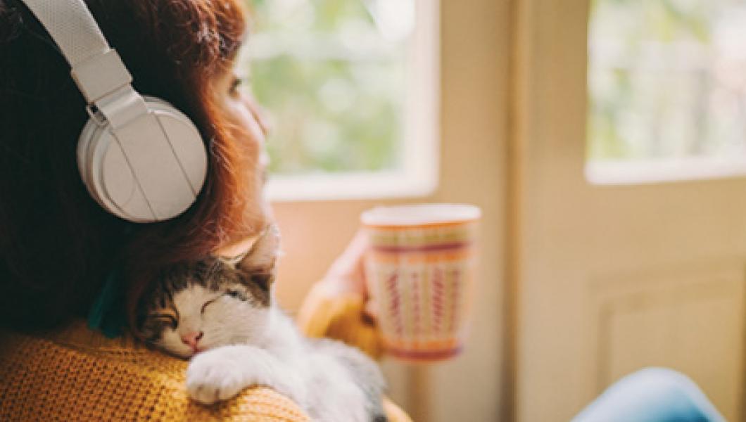 Woman enjoying music, cat, and beverage