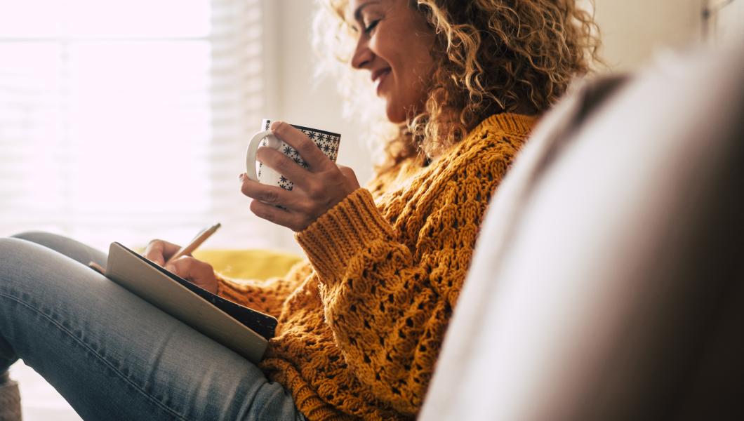 woman on sofa enjoying a cup of coffee and writing 