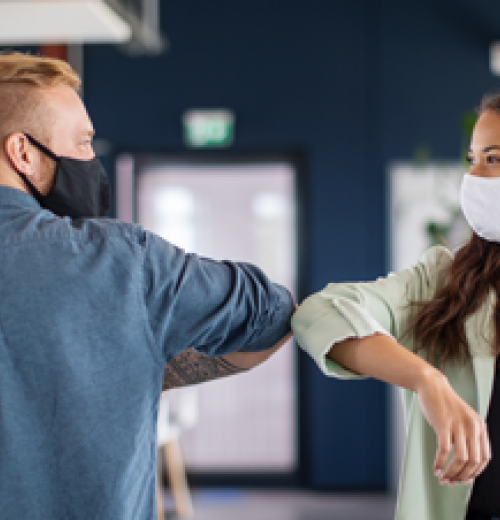 Coworkers bumping elbows and wearing masks