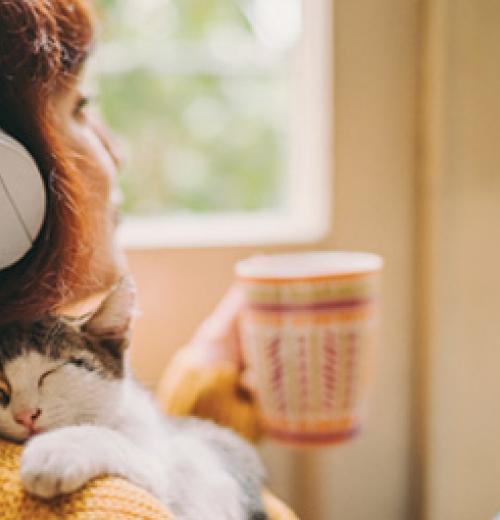 Woman enjoying music, cat, and beverage