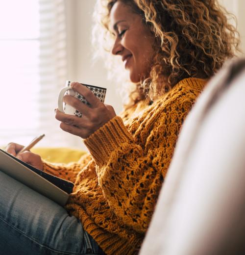 woman on sofa enjoying a cup of coffee and writing 